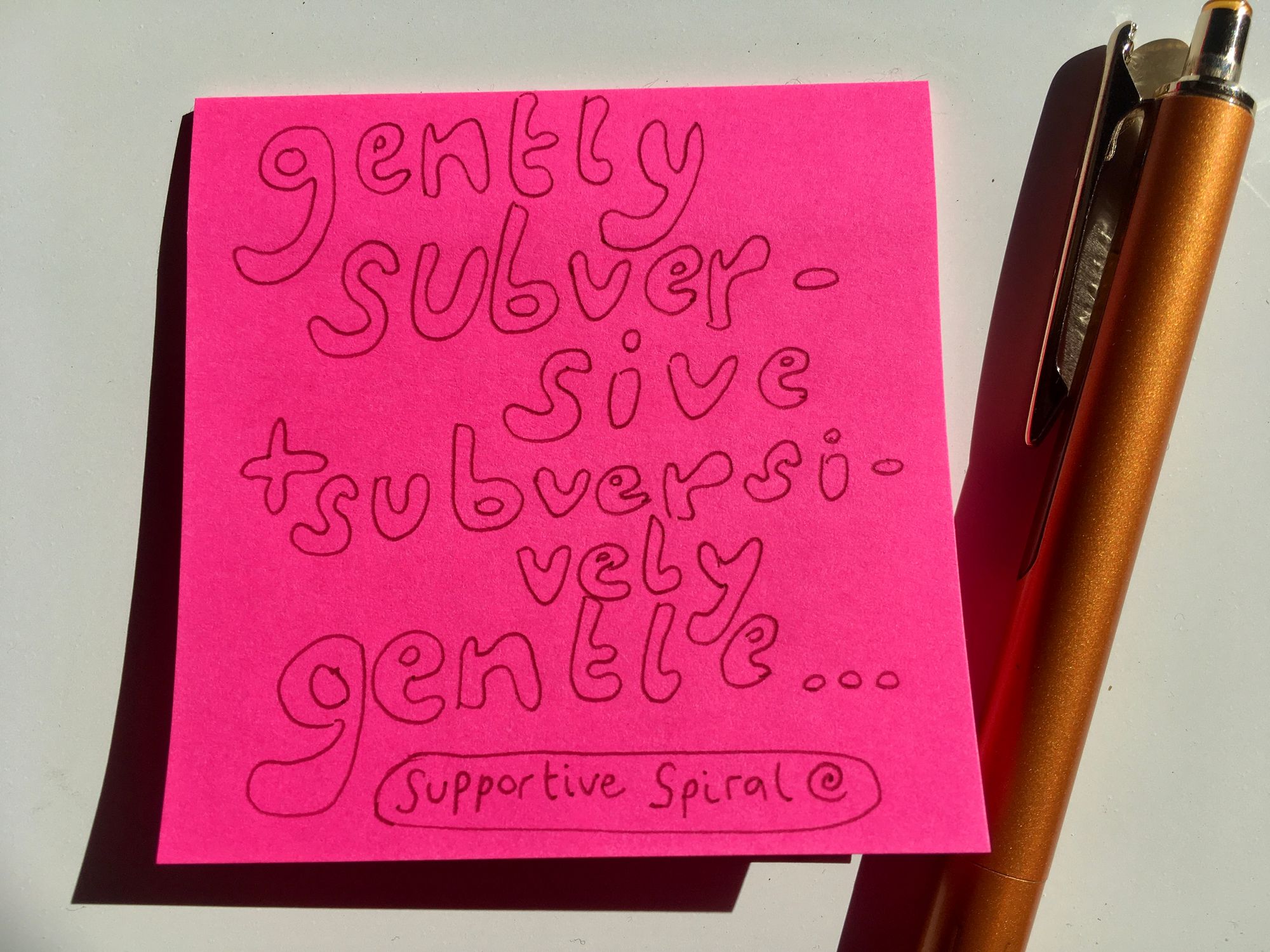 pink sticky note with 'gently subversive + subversively gentle.. Supportive Spiral' hand written on note in bubble letter, gold pen sitting at the right of sticky note